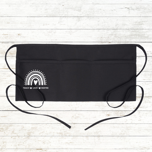 Add a dash of style and inspiration to your teaching wardrobe with this Boho Rainbow Teacher Apron. Featuring a white Boho rainbow design and the motivational phrase "Teach, Love, Inspire", this black apron is perfect for teachers, school aides, or anyone working in an educational setting. With 3 front pockets for easy access to supplies, this apron is both functional and stylish. Personalize it with your name or initials for a custom touch!
