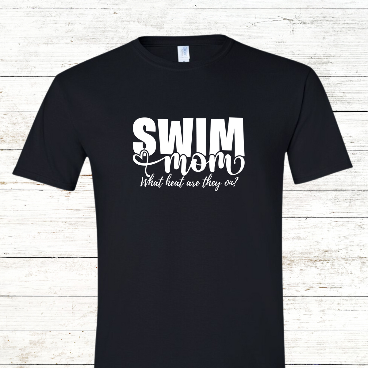 A stylish Swim Mom shirt with the phrase "What Heat Are They On?" printed in bold, eye-catching text across the front. Designed for comfort and humor, it’s perfect for wearing at swim meets while keeping track of events and cheering from the stands.